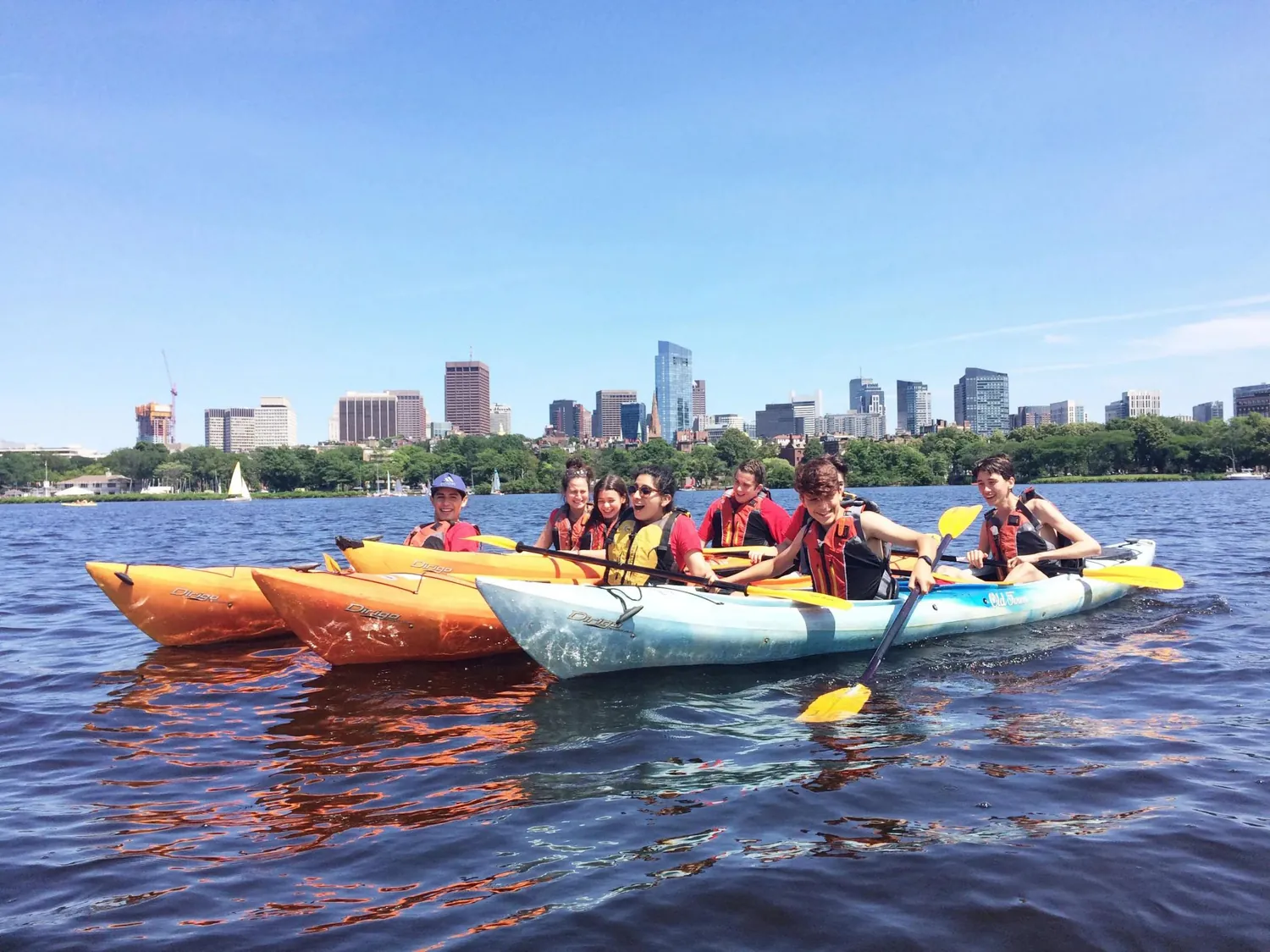 Richi Camp students kayaking on the Charles River with the Boston skyline behind them